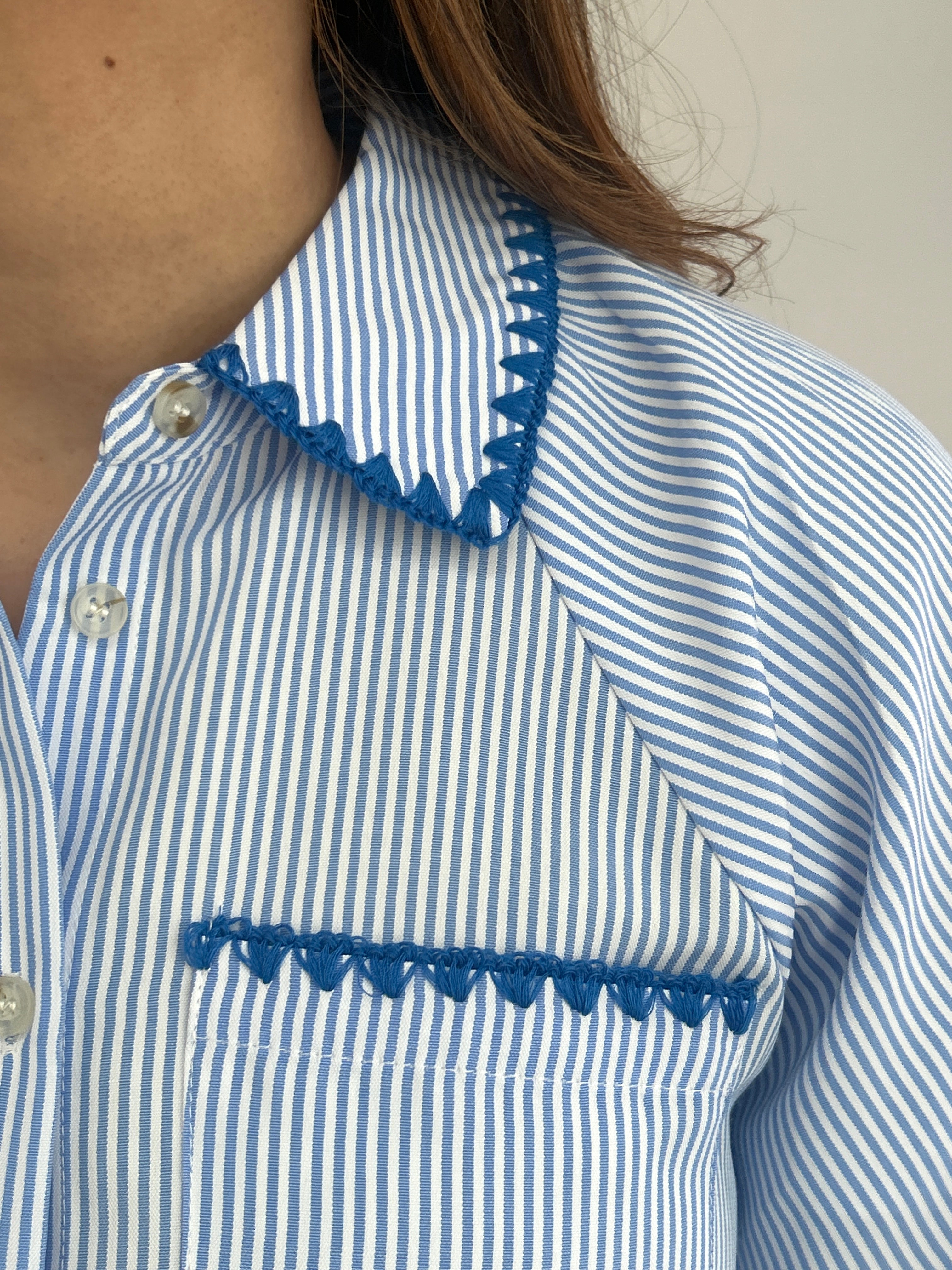 Close-up of a blue and white striped shirt with decorative trim on a neutral background