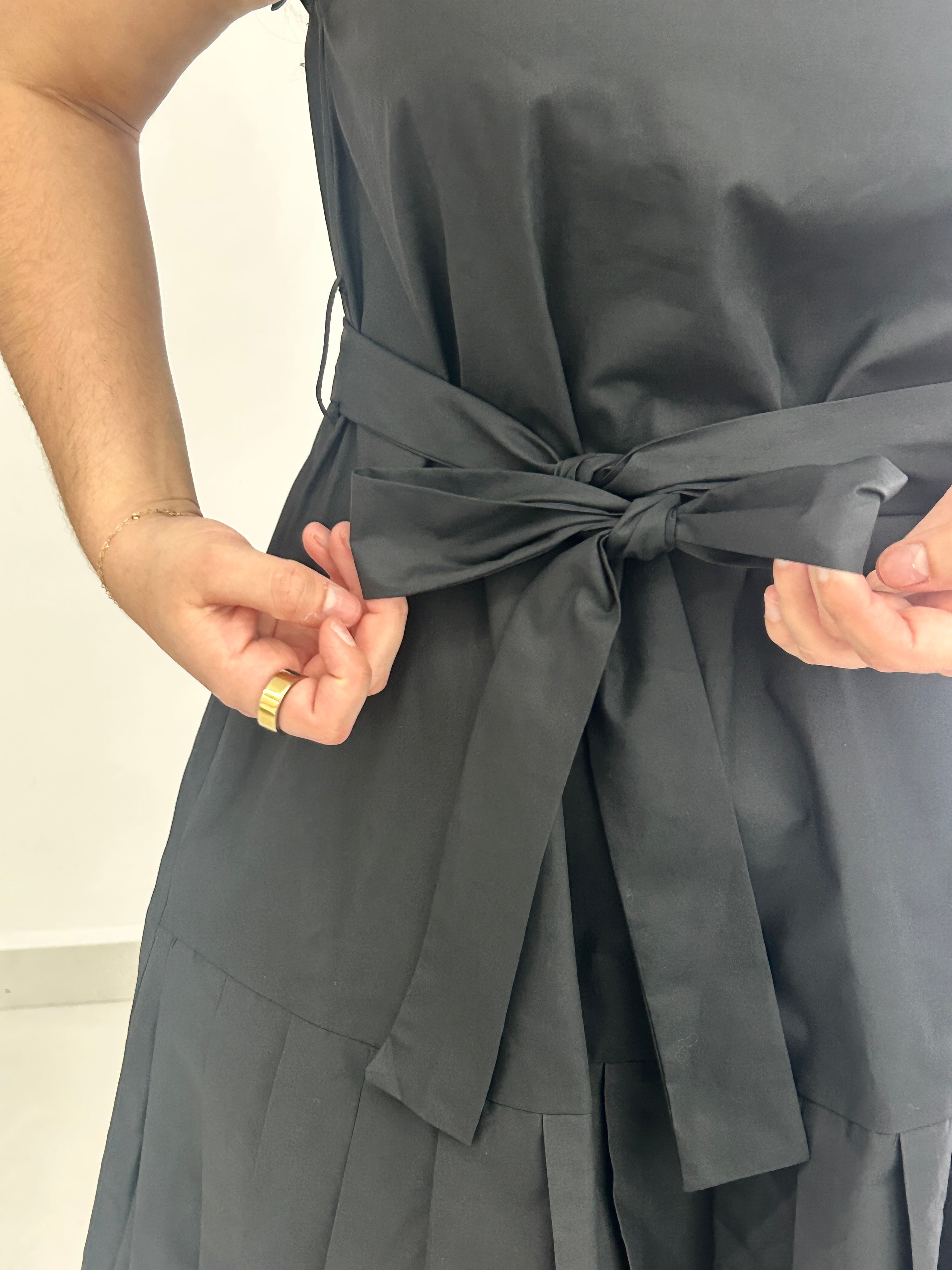 Person wearing a black dress with a tied waist, holding the belt.