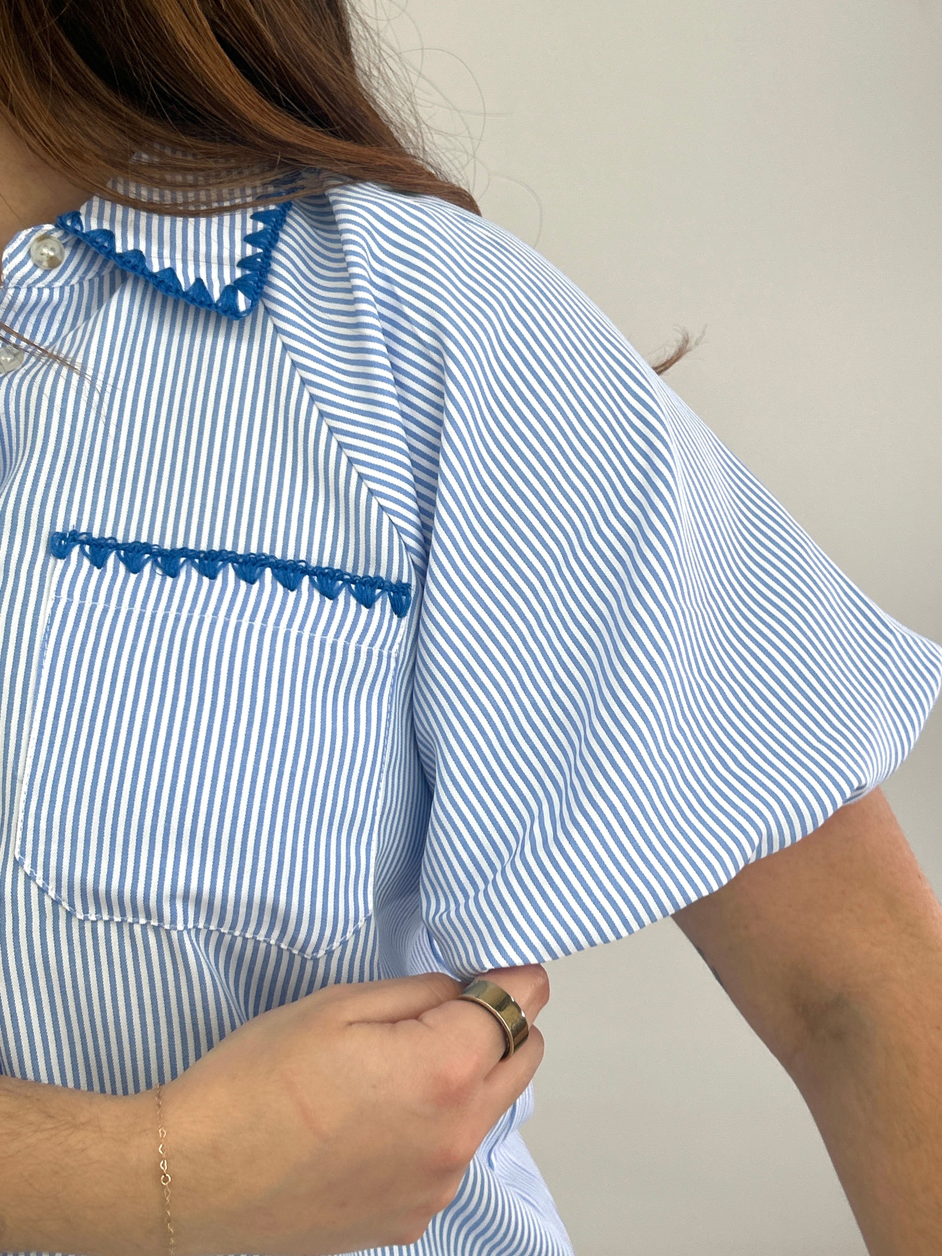 Person wearing a blue and white striped shirt with lace details on a plain background