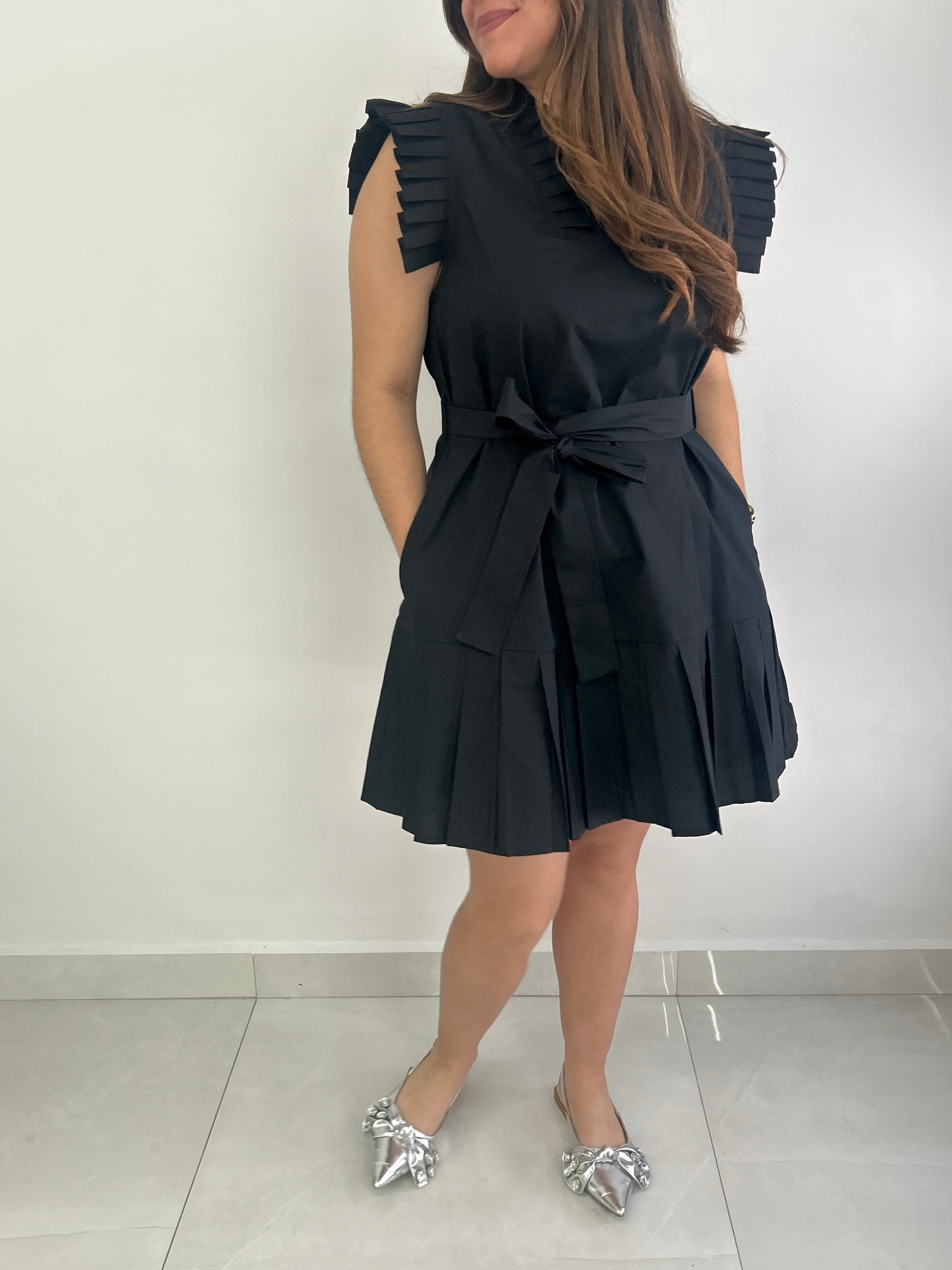 Woman wearing a black dress with ruffled shoulders against a white background