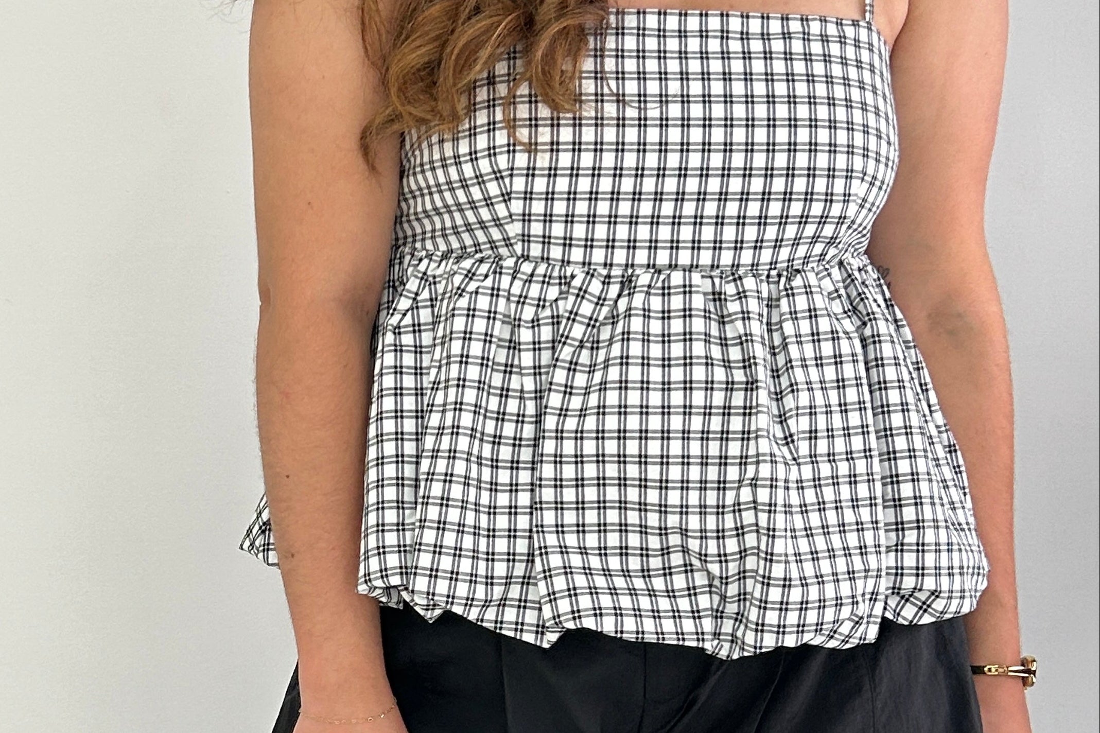 Woman wearing a black and white checkered top and black pants against a plain background