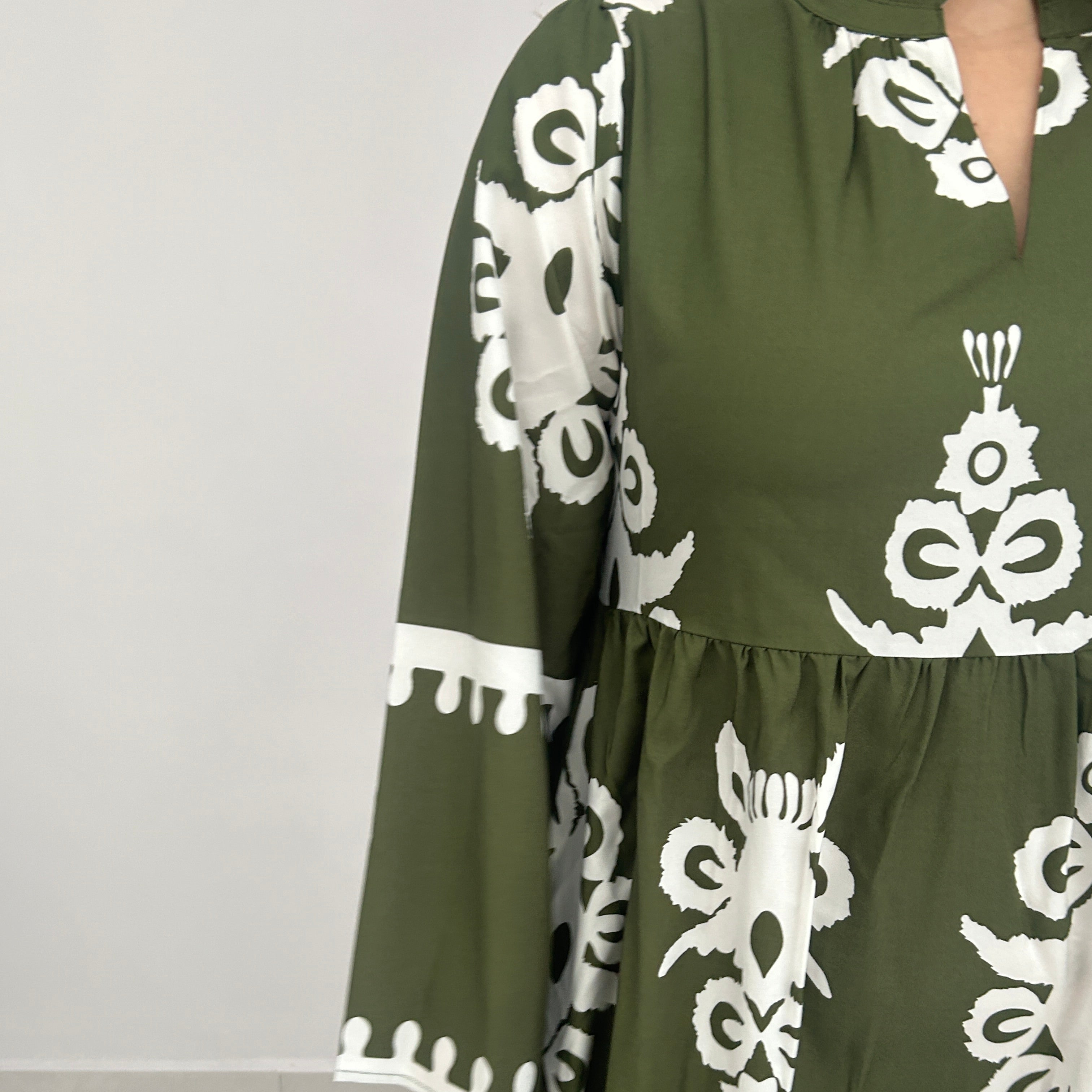 Green garment with white floral patterns held by a person on a light gray background