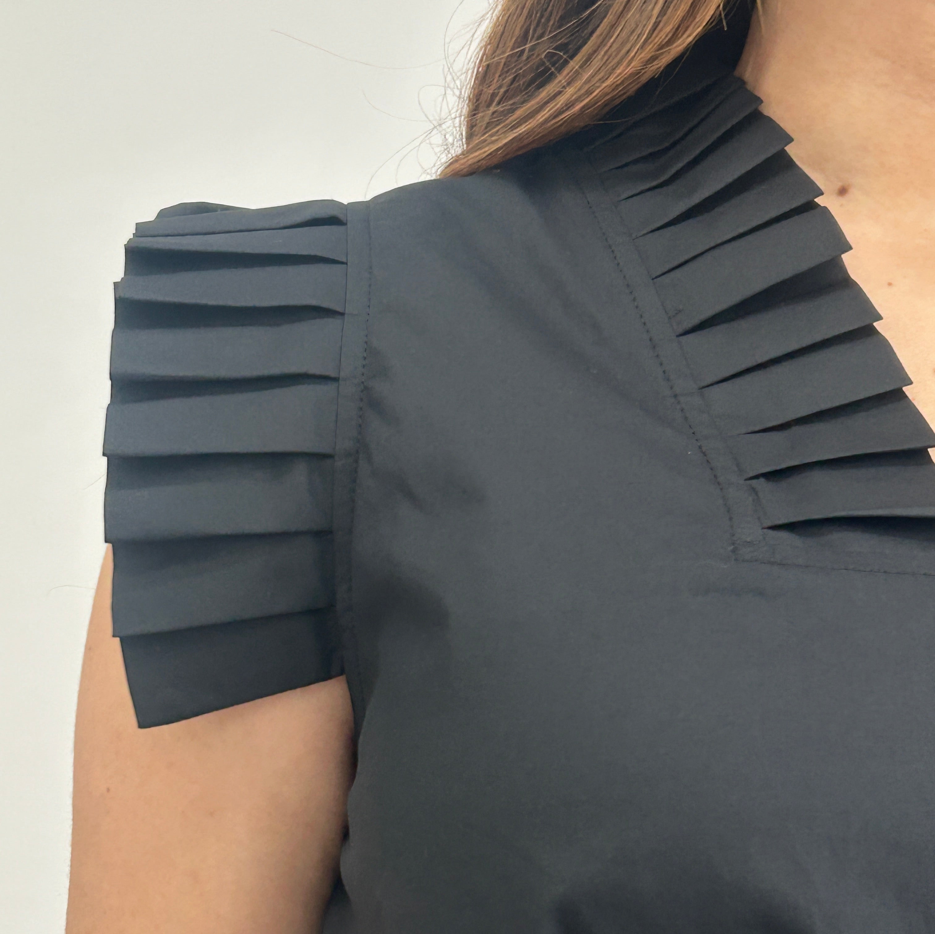 Black pleated top worn by a person on a light background