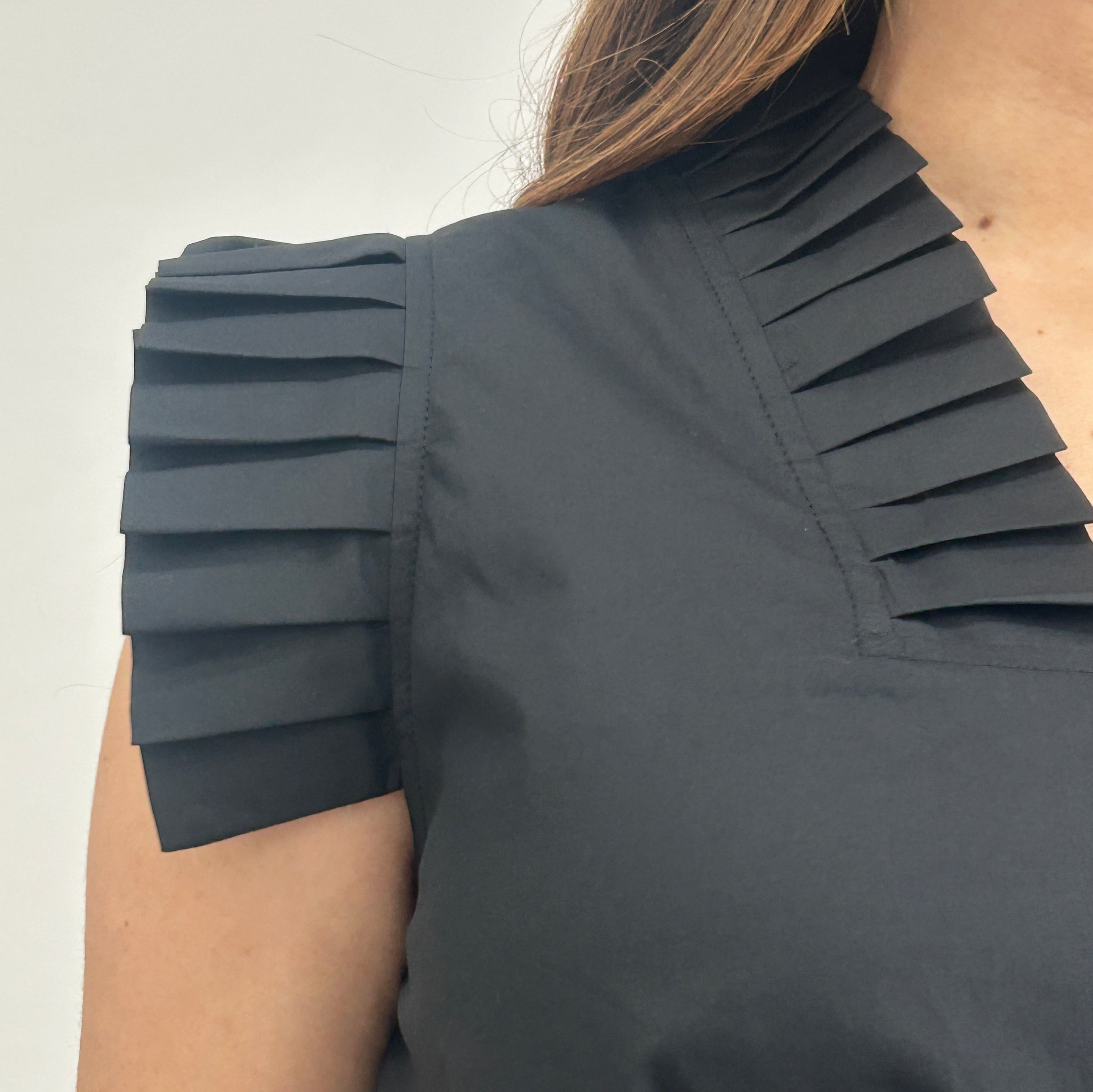 Black pleated top worn by a person on a light background