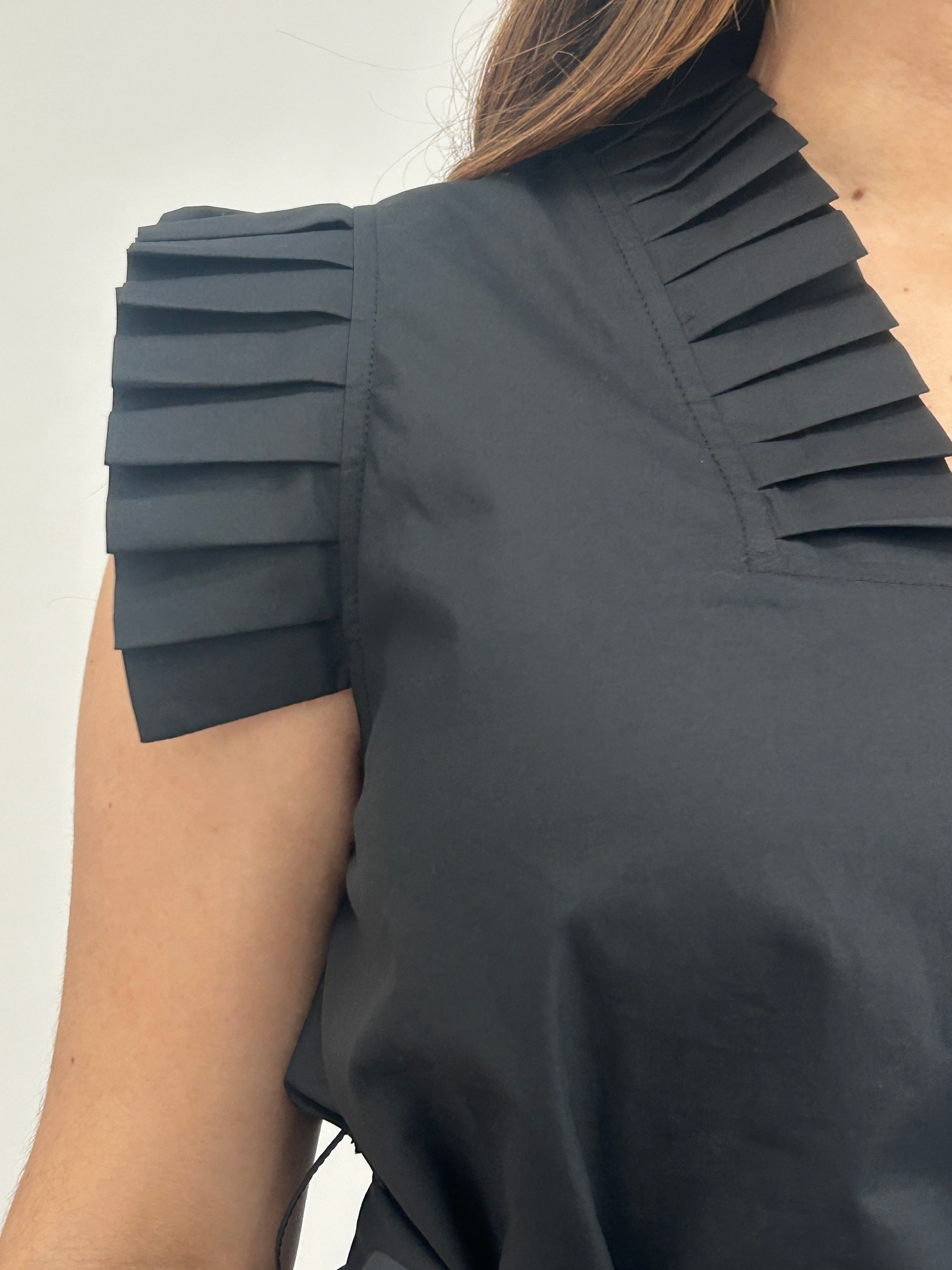 Black pleated top worn by a person on a light background
