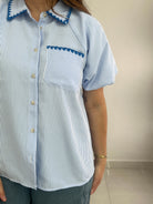 Person wearing a blue and white striped shirt with decorative trim on a plain background