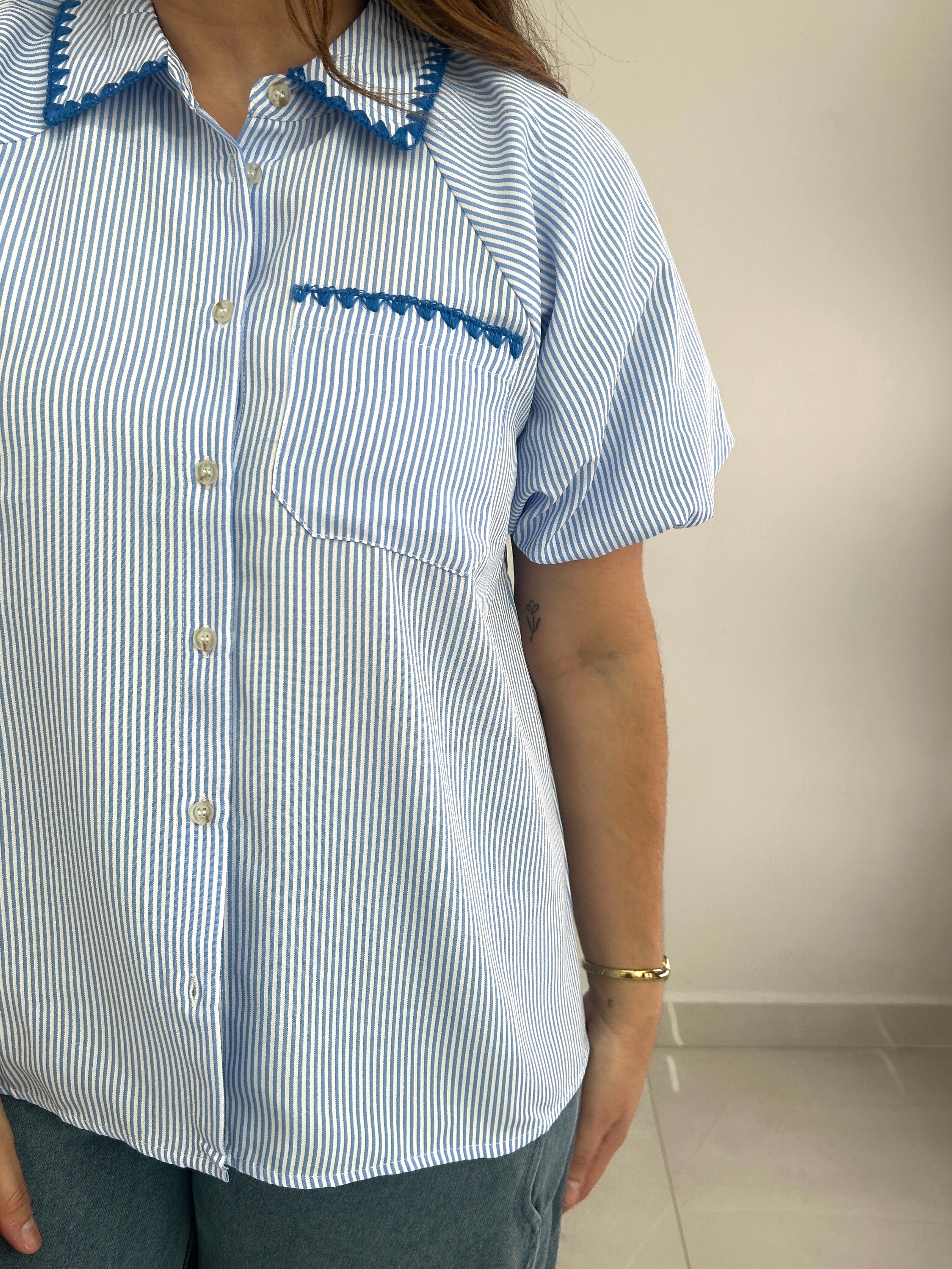Person wearing a blue and white striped shirt with decorative trim on a plain background