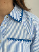 Close-up of a blue and white striped shirt with decorative trim on a neutral background