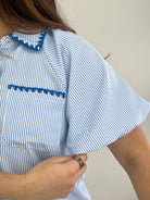Person wearing a blue and white striped shirt with lace details on a plain background