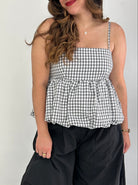 Woman wearing a black and white checkered top and black pants against a plain background