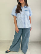 Person wearing a light blue striped shirt and wide-leg jeans against a plain background